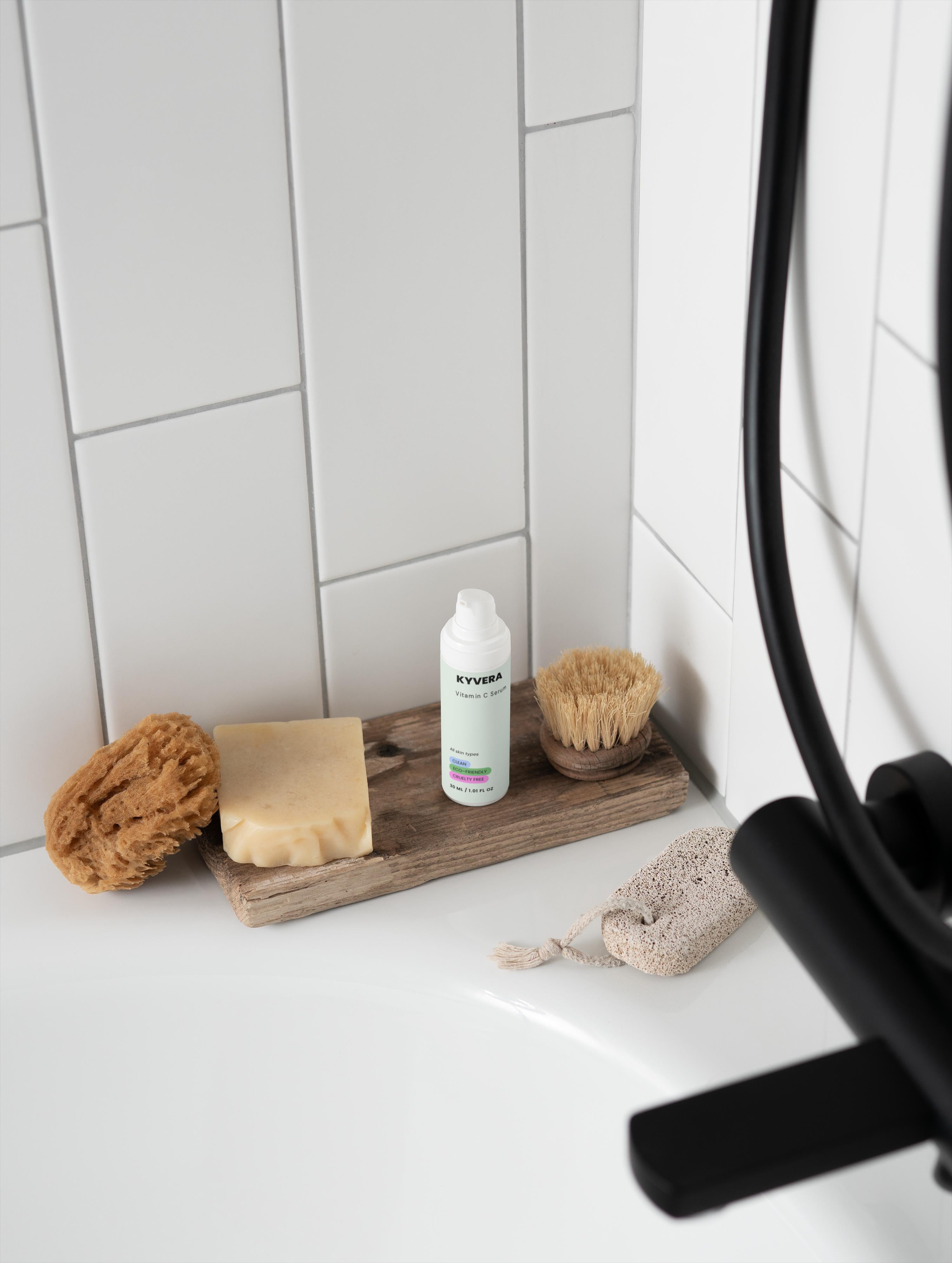 Vitamin C Serum placed beside natural sponges and a soap bar on a wooden tray in a minimalistic bathroom.